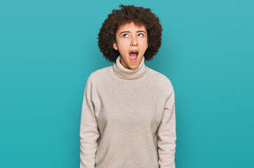 Young hispanic girl wearing wool winter sweater angry and mad screaming frustrated and furious,...