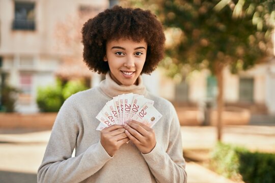 Young hispanic girl smiling happy holding israel shekels at the city.