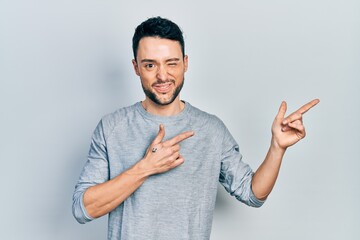 Young hispanic man pointing with fingers to the side winking looking at the camera with sexy...