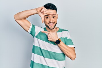 Young hispanic man wearing casual clothes smiling making frame with hands and fingers with happy face. creativity and photography concept.