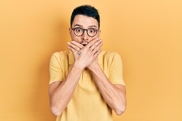 Young hispanic man wearing casual clothes and glasses shocked covering mouth with hands for...