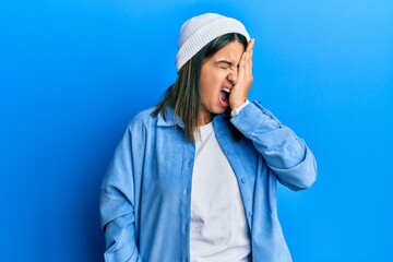Young latin woman wearing cute wool cap yawning tired covering half face, eye and mouth with hand. face hurts in pain.