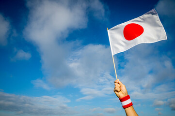 Hand holding Japanese red and white wristband holding national flag of Japan waving in bright sunny...
