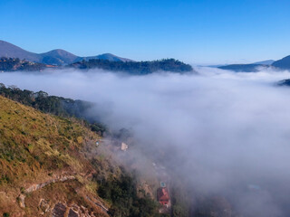 Aerial view of Itaipava, Petrópolis. Early morning with a lot of fog in the city. Mountains with blue sky and clouds around Petrópolis, mountainous region of Rio de Janeiro, Brazil. Drone photo. 
