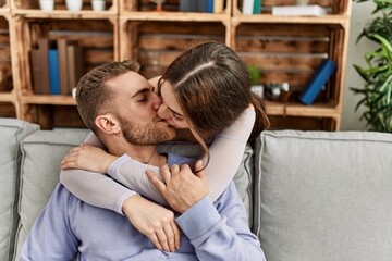 Young caucasian couple sitting on the sofa hugging and kissing at home.