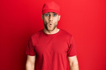 Young caucasian man wearing delivery uniform and cap scared and amazed with open mouth for surprise, disbelief face
