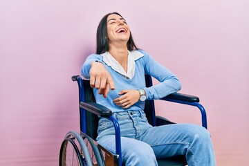 Beautiful woman with blue eyes sitting on wheelchair laughing at you, pointing finger to the camera...