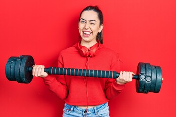 Beautiful woman with blue eyes wearing sportswear using dumbbells winking looking at the camera...