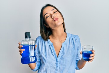 Young hispanic girl holding mouthwash for fresh breath looking at the camera blowing a kiss being lovely and sexy. love expression. - obrazy, fototapety, plakaty
