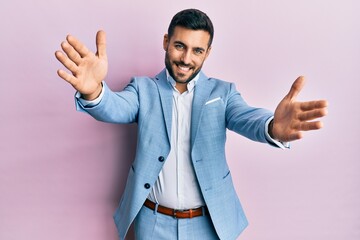Young hispanic businessman wearing business jacket looking at the camera smiling with open arms for...