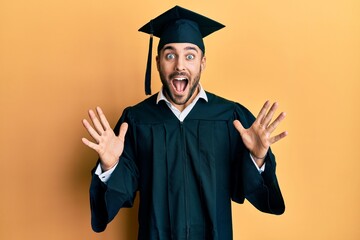 Young hispanic man wearing graduation cap and ceremony robe celebrating crazy and amazed for...