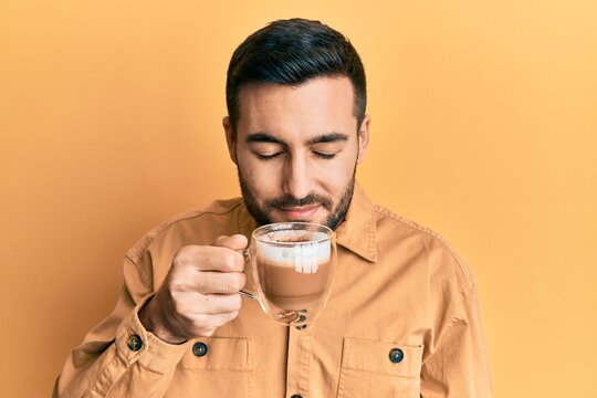 Handsome hispanic man enjoying a cup of coffee over yellow background