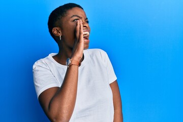 Young african american woman wearing casual white t shirt shouting and screaming loud to side with hand on mouth. communication concept.