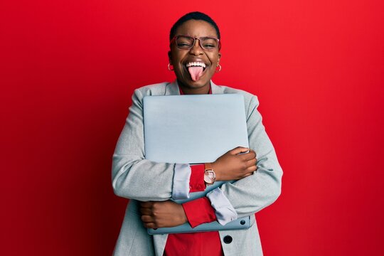 Young african american businesswoman holding laptop sticking tongue out happy with funny expression.
