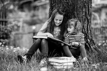 Little sisters reading the book in the summer park. Black and white photo.