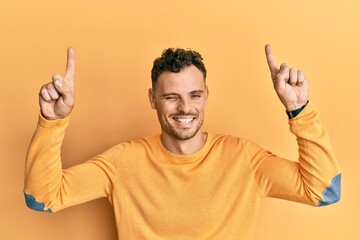 Young hispanic man pointing up with fingers winking looking at the camera with sexy expression,...