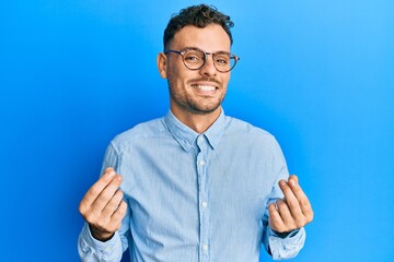 Young hispanic man wearing casual clothes and glasses doing money gesture with hands, asking for...