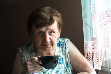 Portrait of an old woman drink tea at her home.