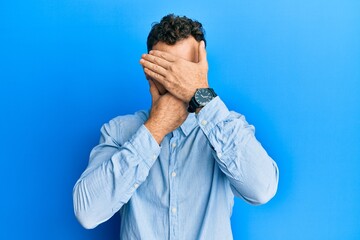Young hispanic man wearing casual clothes and glasses covering eyes and mouth with hands, surprised and shocked. hiding emotion