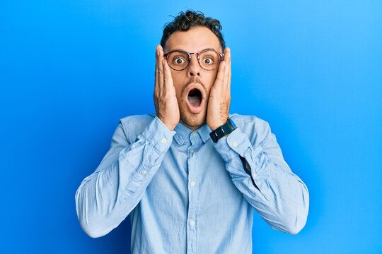 Young hispanic man wearing casual clothes and glasses afraid and shocked, surprise and amazed expression with hands on face