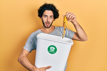 Handsome hispanic man recycling banana peel composting organic fertilizer in shock face, looking...