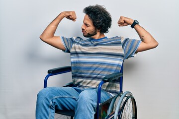 Handsome hispanic man sitting on wheelchair showing arms muscles smiling proud. fitness concept.
