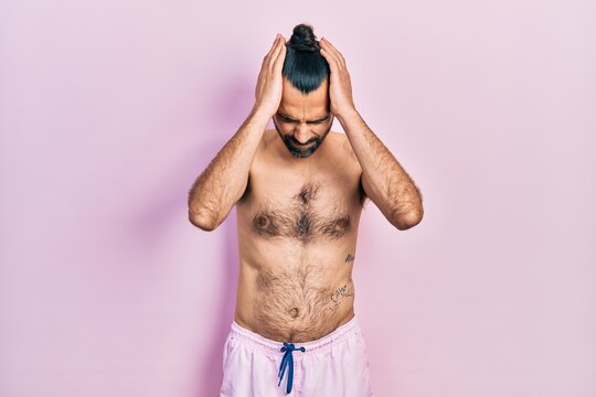 Young hispanic man shirtless wearing swimsuit suffering from headache desperate and stressed because pain and migraine. hands on head.