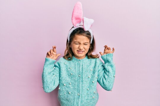 Little beautiful girl wearing cute easter bunny ears gesturing finger crossed smiling with hope and eyes closed. luck and superstitious concept.