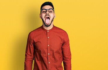 Young hispanic man with beard wearing business shirt and glasses sticking tongue out happy with funny expression. emotion concept.