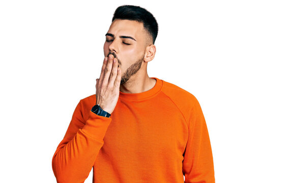 Young hispanic man with beard wearing casual orange sweater bored yawning tired covering mouth with hand. restless and sleepiness.