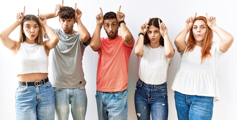 Fototapeta premium Group of young friends standing together over isolated background doing funny gesture with finger over head as bull horns