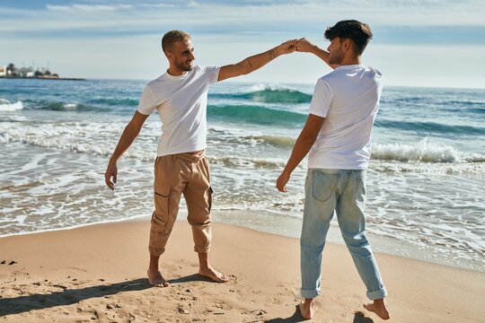Young gay couple smiling happy dancing at the beach.