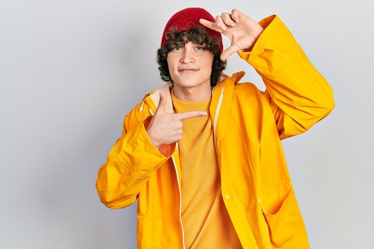 Handsome young man wearing yellow raincoat smiling making frame with hands and fingers with happy face. creativity and photography concept.