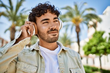 Handsome hispanic man with beard smiling happy outdoors on a sunny day wearing headphones