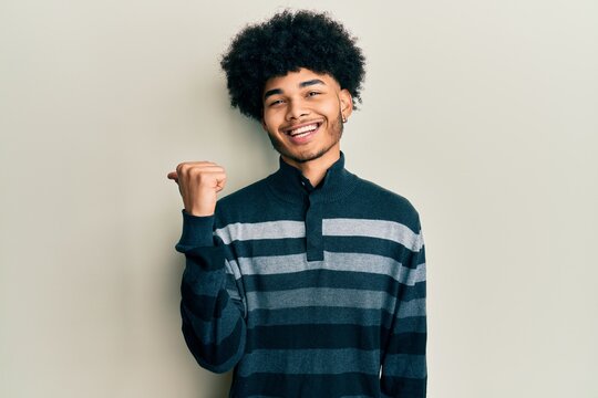 Young african american man with afro hair wearing casual clothes smiling with happy face looking and pointing to the side with thumb up.