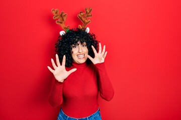 Young middle east woman wearing cute christmas reindeer horns afraid and terrified with fear expression stop gesture with hands, shouting in shock. panic concept.