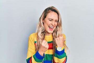 Beautiful young blonde woman wearing colored sweater celebrating surprised and amazed for success with arms raised and eyes closed. winner concept.