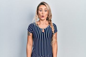 Beautiful young blonde woman wearing casual striped dress afraid and shocked with surprise expression, fear and excited face.
