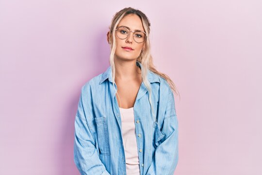 Beautiful young blonde woman wearing casual clothes and glasses relaxed with serious expression on face. simple and natural looking at the camera.