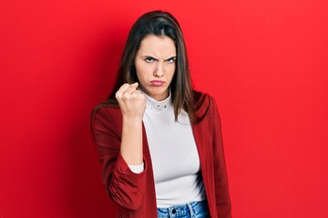 Young brunette teenager wearing business jacket angry and mad raising fist frustrated and furious...