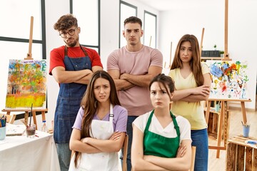 Group of five hispanic artists at art studio skeptic and nervous, disapproving expression on face with crossed arms. negative person.