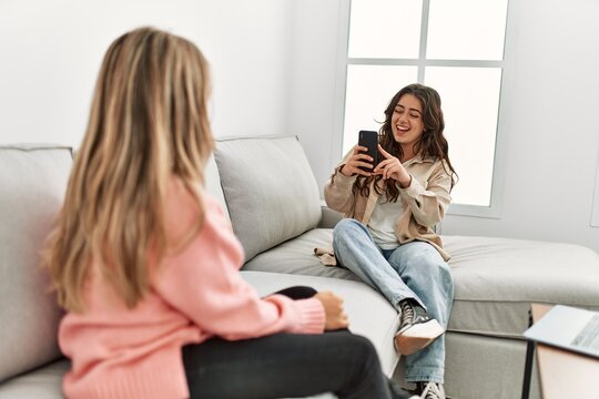 Young woman making picture of her girlfriend using smartphone at home