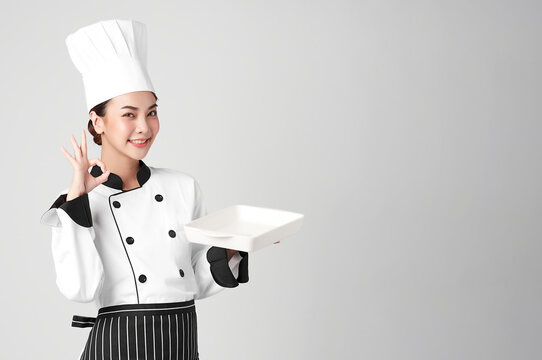 Beautiful young asian woman chef holding empty white plate on white background.