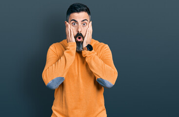 Hispanic man with beard wearing casual winter sweater afraid and shocked, surprise and amazed expression with hands on face