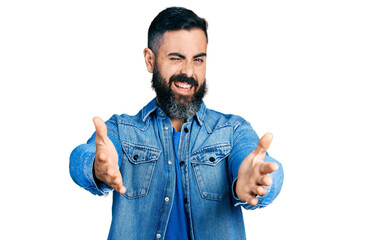 Hispanic man with beard with open arms doing hug gesture winking looking at the camera with sexy expression, cheerful and happy face.