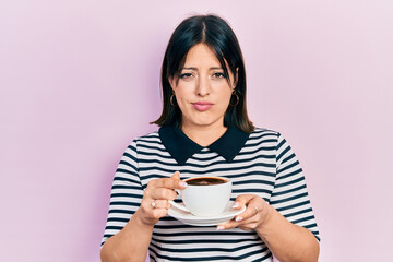 Young hispanic woman drinking a cup of coffee skeptic and nervous, frowning upset because of problem. negative person.