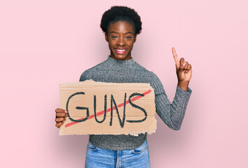 Young african american girl holding no guns warning banner surprised with an idea or question pointing finger with happy face, number one