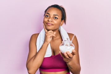 Young african american girl wearing sportswear holding sugar serious face thinking about question with hand on chin, thoughtful about confusing idea