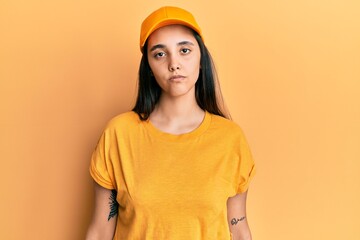 Young hispanic woman wearing delivery uniform and cap relaxed with serious expression on face. simple and natural looking at the camera.