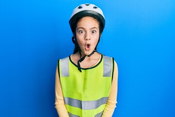 Beautiful brunette little girl wearing bike helmet and reflective vest afraid and shocked with surprise expression, fear and excited face.